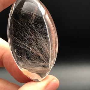 May include: A clear quartz crystal with a unique inclusion of black rutile, creating a beautiful, natural, and intricate design. The crystal is shaped like an oval and has a smooth, polished surface.