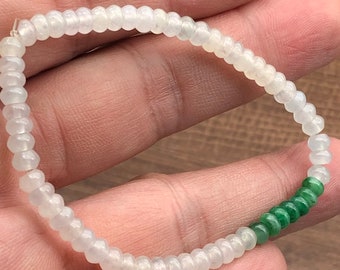 Pode incluir: Um bracelete de jade branco com detalhes em jade verde. O bracelete é feito de pequenas contas redondas.