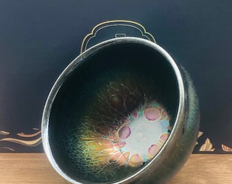 Puede incluir: Una taza de té de cerámica verde oscuro con un esmalte metálico iridiscente. El esmalte tiene un patrón de remolino de oro, verde y rosa.