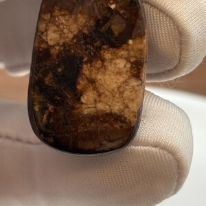 Puede incluir: Un colgante de oro con una piedra marr&oacute;n y blanca. La piedra tiene un patr&oacute;n de m&aacute;rmol.