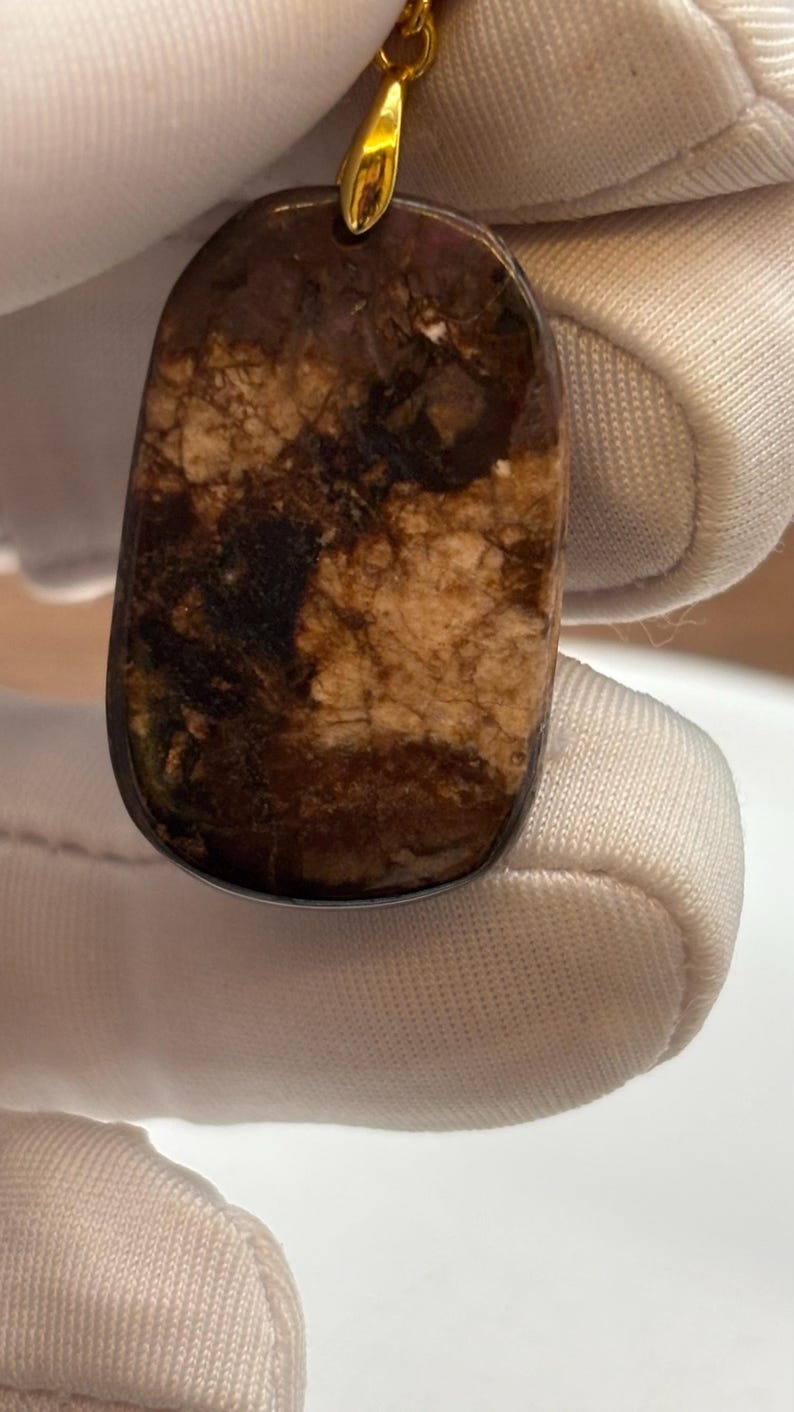 Puede incluir: Un colgante de oro con una piedra marr&oacute;n y blanca. La piedra tiene un patr&oacute;n de m&aacute;rmol.