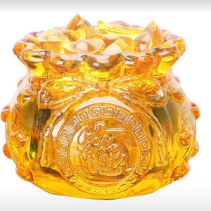 Puede incluir: Una escultura de vidrio dorado de una bolsa de dinero que rebosa de monedas. La bolsa está decorada con detalles intrincados y un diseño circular con caracteres chinos.