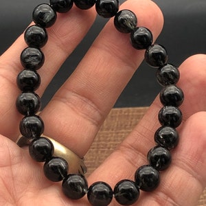 Op de afbeelding: Zwarte kralen armband met zilveren vlekken. De armband is gemaakt van ronde kralen en is geregen op een elastisch koord.