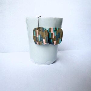 May include: A pair of square dangle earrings with a geometric pattern in shades of brown, blue, and pink.