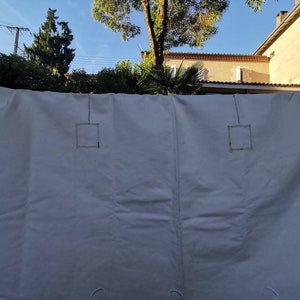 May include: White linen tablecloth with embroidered squares and a delicate lace trim. The tablecloth is hanging on a clothesline outdoors.