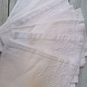 May include: A stack of white linen napkins with embroidered floral designs. The napkins are folded and arranged in a fan shape.