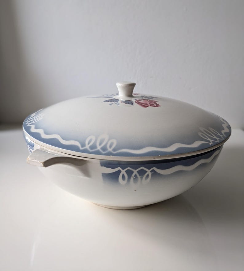 Puede incluir: Un taz&oacute;n de servir de cer&aacute;mica blanca con un dise&ntilde;o floral azul y blanco. El taz&oacute;n tiene una tapa con un pomo en la parte superior.