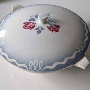 Puede incluir: Un plato de servir de cer&aacute;mica blanca con un dise&ntilde;o floral azul y blanco. El plato tiene dos asas y una tapa.
