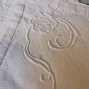May include: White linen fabric with a delicate embroidered floral design. The embroidery is raised and creates a textured effect.