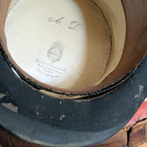Pu&ograve; includere: Un cilindro con una fascia esterna nera e una fodera interna di colore chiaro. L'interno presenta le iniziali A. D. e un'etichetta stampata con la scritta Manufacture de Chapeaux Berteil, 18 Rue de Lang Comedie Paris, Medailles Dor 1878-1889.