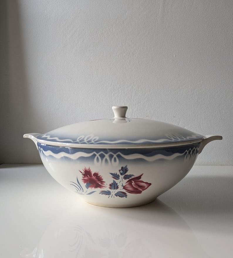 Puede incluir: Un taz&oacute;n de servir de cer&aacute;mica blanca con tapa, con un dise&ntilde;o floral azul y blanco con acentos rosados. El taz&oacute;n tiene dos asas a los lados.