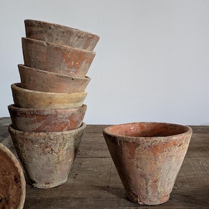 Peut inclure: Ensemble de pots en terre cuite anciens, d'aspect vieilli. Les pots, de tailles et de formes variées, présentent une couleur brun-rouge et des surfaces texturées. Certains sont empilés, d'autres sont posés sur une surface en bois.