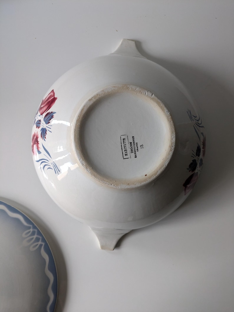 Puede incluir: Taz&oacute;n de servir de cer&aacute;mica blanca con un patr&oacute;n floral azul y rojo. El taz&oacute;n tiene dos asas y en la parte inferior se lee "MADE IN FRANCE, SARREGUEMINES, JAUNE/JAUNE, 58".