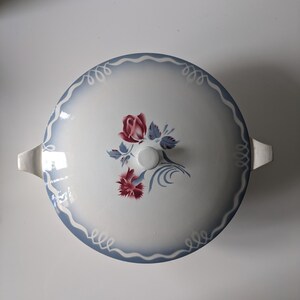 Puede incluir: Plato de servir de cer&aacute;mica blanca con un dise&ntilde;o floral azul y blanco. El plato tiene una tapa con un pomo en la parte superior. El dise&ntilde;o floral presenta rosas rojas y rosas.
