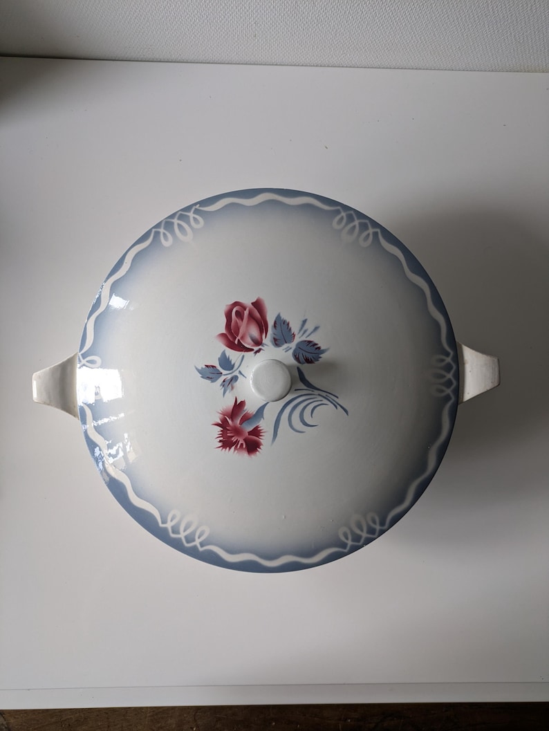 Puede incluir: Plato de servir de cer&aacute;mica blanca con un dise&ntilde;o floral azul y blanco. El plato tiene una tapa con un pomo en la parte superior. El dise&ntilde;o floral presenta rosas rojas y rosas.