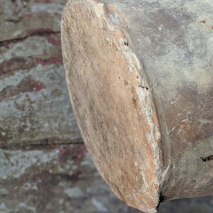 May include: Close-up of a weathered, cylindrical wooden object with a rough, textured surface. The end of the cylinder is visible, showing a lighter, worn area. The wood has a natural, aged appearance.