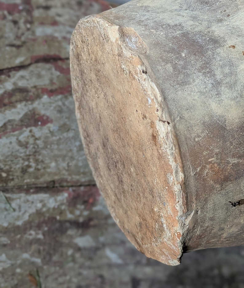 May include: Close-up of a weathered, cylindrical wooden object with a rough, textured surface. The end of the cylinder is visible, showing a lighter, worn area. The wood has a natural, aged appearance.