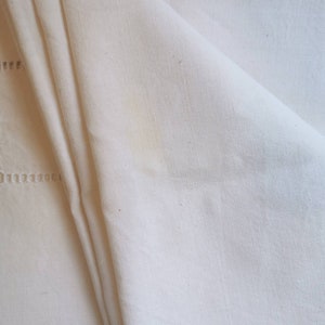 May include: A white linen tablecloth with a delicate embroidered border. The fabric is soft and textured, with a subtle sheen.