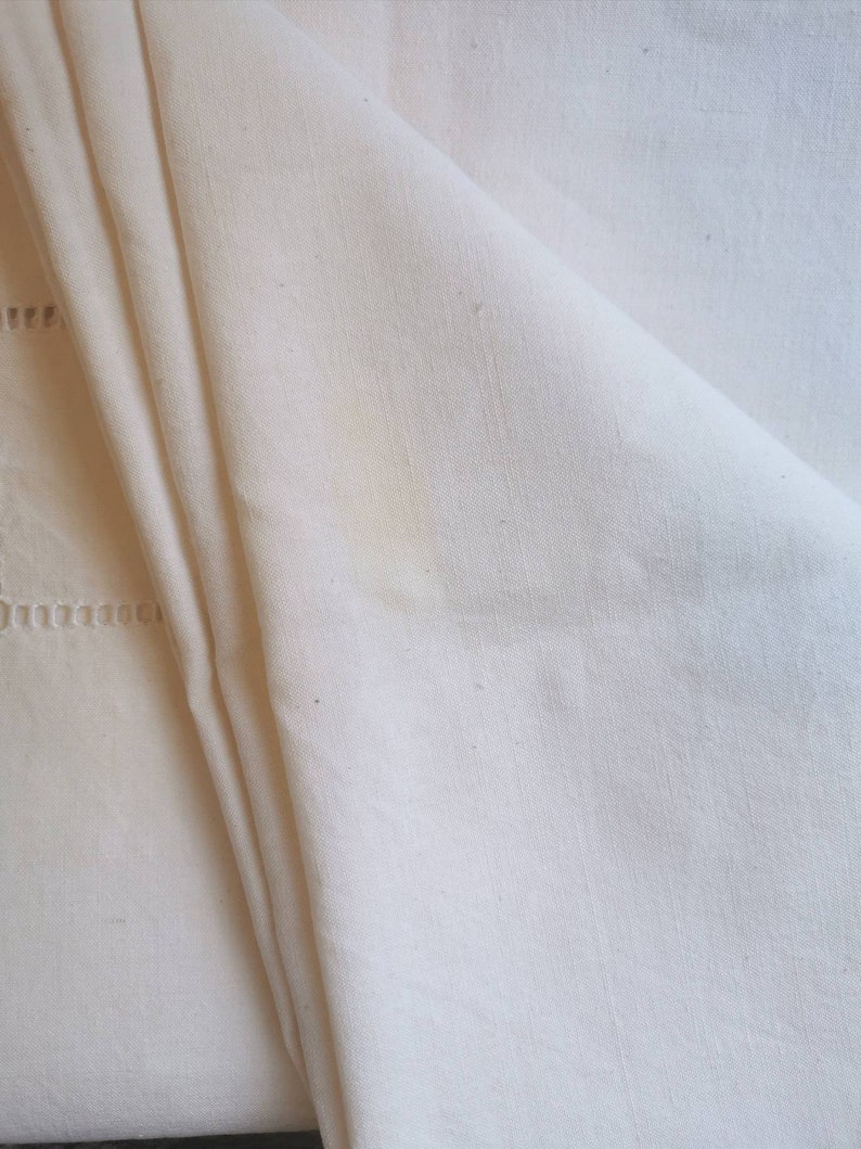 May include: A white linen tablecloth with a delicate embroidered border. The fabric is soft and textured, with a subtle sheen.