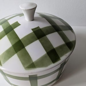 May include: A white ceramic serving dish with a lid, featuring a green plaid pattern. The lid has a small, white knob. The dish is designed for serving food and adds a touch of vintage charm to any table setting.