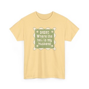 Könnte beinhalten: Hellgelbes T-Shirt mit einem grün-weißen Aufdruck mit der Aufschrift "BABY! Where the hell is my Husband". Die Grafik hat eine quadratische Form mit einem gewellten Rand und kleinen sternförmigen Designs.