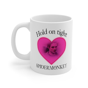 May include: White ceramic mug with a pink heart design, a portrait, and the text "Hold on tight SPIDERMONKEY". The mug has a curved handle and a glossy finish. A fun gift for fans.