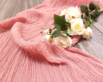 Könnte beinhalten: Ein rosa gekräuselter Stoffläufer mit weißen Rosen darauf. Der Stoff ist weich und strukturiert, und die Rosen sind zart und schön.