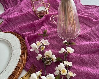 Könnte beinhalten: Ein lilafarbener Tischläufer mit einem weißen Blumenzweig, einem goldenen Kerzenhalter und einer durchsichtigen Glasvase mit getrockneten Blumen.