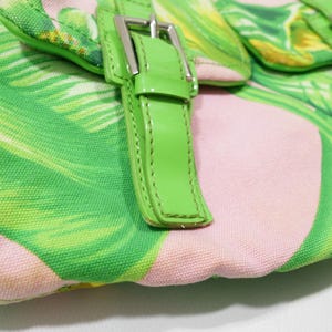K&ouml;nnte beinhalten: Nahaufnahme einer Handtasche mit tropischem Bl&auml;ttermuster in Gr&uuml;n und Rosa. Die Tasche hat leuchtend gr&uuml;ne Lederriemen und silberne Schnallen. Der Stoff hat eine leinwandartige Textur.