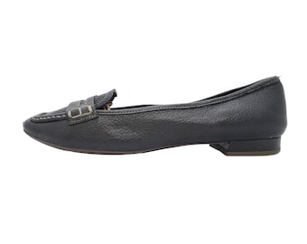 May include: A dark grey leather loafer-style flat shoe. The shoe has a textured surface, a decorative strap with a buckle, and a small heel. Stitching is visible around the toe and the strap.