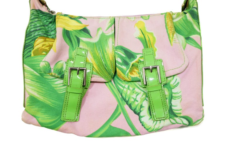 K&ouml;nnte beinhalten: Rosa Umh&auml;ngetasche mit tropischem Blattmuster in Gr&uuml;n und Gelb. Die Tasche hat zwei Vordertaschen mit hellgr&uuml;nen Schnallenverschl&uuml;ssen und einer silbernen Metallschnalle. Sie hat einen Schulterriemen.