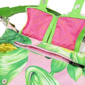 K&ouml;nnte beinhalten: Versus Versace Handtasche mit tropischem Blattmuster in Rosa und Gr&uuml;n. Die Tasche hat ein rosa Innenfutter mit dem Versus-Logo, einen gr&uuml;nen Riemen und einen rosa Rei&szlig;verschluss. Die Tasche ist mit einem Schulterriemen ausgestattet.