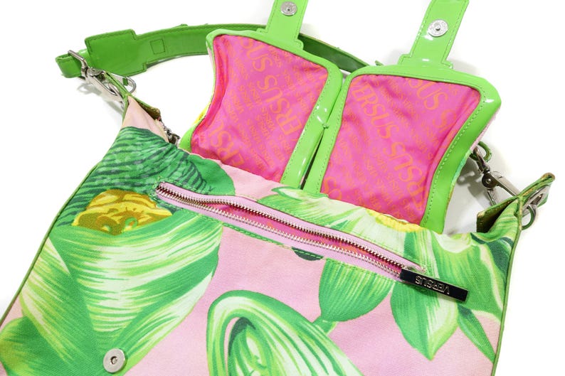 K&ouml;nnte beinhalten: Versus Versace Handtasche mit tropischem Blattmuster in Rosa und Gr&uuml;n. Die Tasche hat ein rosa Innenfutter mit dem Versus-Logo, einen gr&uuml;nen Riemen und einen rosa Rei&szlig;verschluss. Die Tasche ist mit einem Schulterriemen ausgestattet.