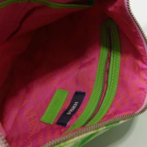 K&ouml;nnte beinhalten: Innenansicht einer Versus Handtasche. Die Tasche hat ein leuchtend pinkfarbenes Innenfutter mit einem gr&uuml;nen Rei&szlig;verschluss und Zierleisten. Die Au&szlig;enseite hat ein Blumenmuster. Ein kleines Etikett mit dem Wort "VERSUS" ist im Inneren sichtbar.