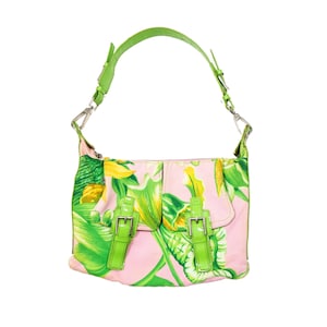K&ouml;nnte beinhalten: Eine rosa Umh&auml;ngetasche mit einem gr&uuml;nen und gelben Blumenmuster. Die Tasche hat einen gr&uuml;nen Henkel und zwei gr&uuml;ne Schnallenverschl&uuml;sse auf der Vorderseite. Die Tasche ist aus weichem Material.
