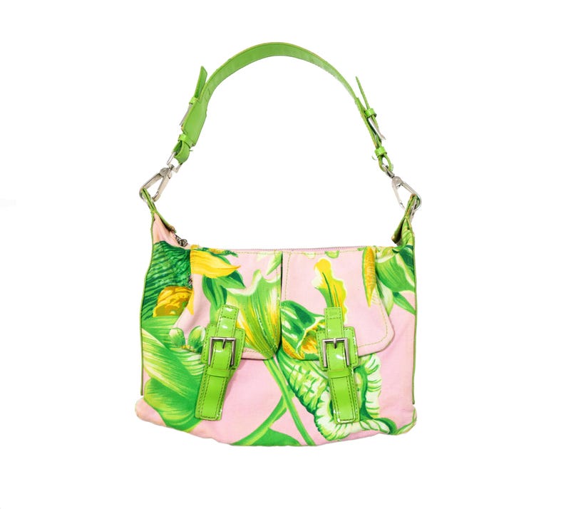 K&ouml;nnte beinhalten: Eine rosa Umh&auml;ngetasche mit einem gr&uuml;nen und gelben Blumenmuster. Die Tasche hat einen gr&uuml;nen Henkel und zwei gr&uuml;ne Schnallenverschl&uuml;sse auf der Vorderseite. Die Tasche ist aus weichem Material.