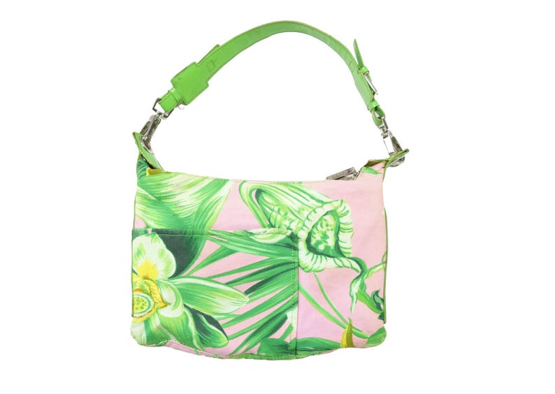K&ouml;nnte beinhalten: Eine rosa Umh&auml;ngetasche mit gr&uuml;nem Blumenmuster und einem leuchtend gr&uuml;nen Riemen. Die Tasche hat eine Vordertasche und silberfarbene Beschl&auml;ge. Das florale Design umfasst gr&uuml;ne Bl&auml;tter und wei&szlig;e und gelbe Bl&uuml;ten.