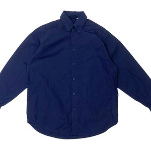 May include: A navy blue button-down shirt with long sleeves. The shirt has a button-down collar, a chest pocket, and buttons down the front. The shirt is made of a solid, dark blue fabric.