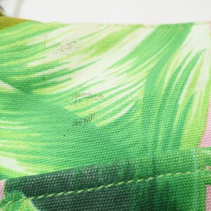 K&ouml;nnte beinhalten: Nahaufnahme eines Teils einer Tasche mit tropischem Bl&auml;ttermuster. Das Design zeigt gro&szlig;e gr&uuml;ne Bl&auml;tter mit wei&szlig;en Akzenten auf einem rosa Hintergrund. Der Stoff der Tasche ist robustes Canvas, und die N&auml;hte sind sichtbar.