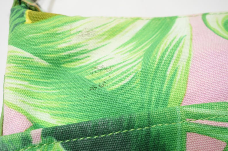 K&ouml;nnte beinhalten: Nahaufnahme eines Teils einer Tasche mit tropischem Bl&auml;ttermuster. Das Design zeigt gro&szlig;e gr&uuml;ne Bl&auml;tter mit wei&szlig;en Akzenten auf einem rosa Hintergrund. Der Stoff der Tasche ist robustes Canvas, und die N&auml;hte sind sichtbar.