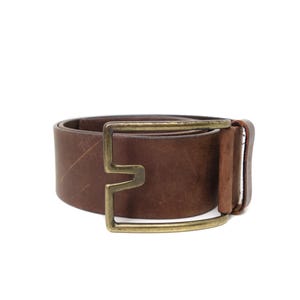 May include: A brown leather belt with a brass-colored buckle. The belt is a medium width and has a simple, classic design. The buckle is a unique shape, adding a touch of style to the belt.