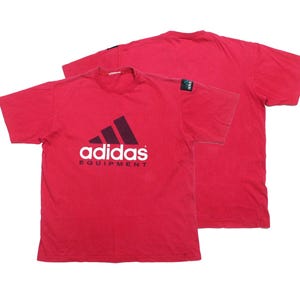 Può includere: T-shirt rosso con il logo Adidas Equipment in bianco e nero. La maglietta a maniche corte ha uno scollo tondo. Il logo Adidas è sul davanti. La maglietta è mostrata davanti e dietro.