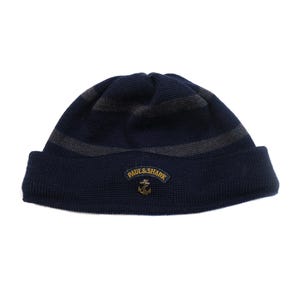 May include: A navy blue knit beanie with two gray stripes and a folded brim. The hat features a small patch with the text "PAUL & SHARK" and an anchor emblem. The beanie is made of a textured knit material.