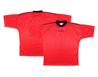 May include: Two red athletic jerseys with black accents. The jerseys have a vertical striped pattern and a black collar. The Adidas logo is visible on the front of one jersey. The jerseys are short-sleeved.