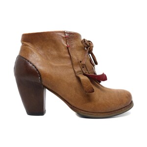 May include: A brown leather ankle boot with a dark brown heel and accents. The boot features a rounded toe, a small red accent, and a lace-up design. The heel measures approximately 3 inches.