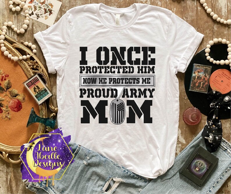 Puede incluir: Camiseta blanca con texto negro que dice "I once protected him now he protects me proud army mom". El texto est&aacute; rodeado de un contorno negro. Una placa de identificaci&oacute;n plateada con una peque&ntilde;a bandera estadounidense cuelga del texto.