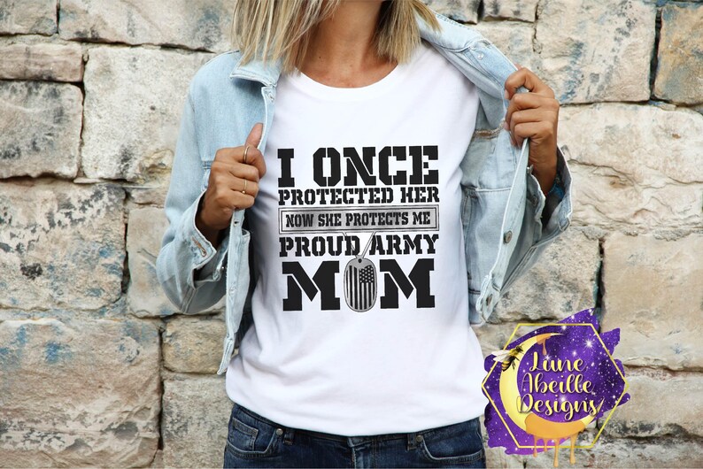 Puede incluir: Camiseta blanca con texto negro que dice "I once protected her now she protects me proud army mom" con un peque&ntilde;o gr&aacute;fico de la bandera estadounidense.