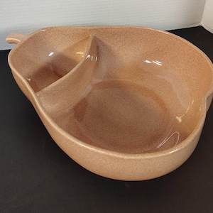 May include: A speckled, pear-shaped serving dish with two compartments. The dish is a warm, earthy tone with a glossy finish. It has a small handle on one side and a divider creating two separate sections for serving snacks or appetizers.