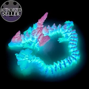 Könnte beinhalten: Eine leuchtende blaue und rosa Drachenskulptur aus Kristallen. Der Drache ist zu einem Kreis zusammengerollt, mit dem Kopf auf dem Schwanz.