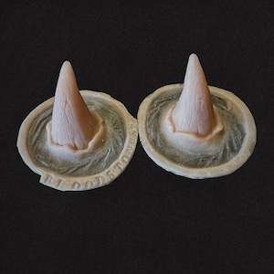 Może przedstawiać: Dwa bladoróżowe, stożkowate obiekty o teksturowanej powierzchni, osadzone na okrągłej podstawie. Podstawa ma teksturowany, półprzezroczysty wygląd. Tekst "BLOODSTONE SETS" jest widoczny na podstawie. Tło jest jednolicie czarne.